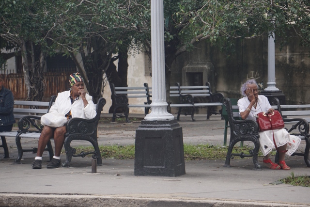 People seated on outdoor benches in Havana, Cuba.